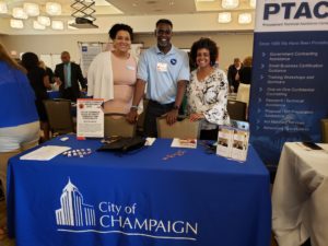 Three people standing behind a City of Champaign table