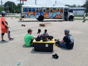 Kids sitting on ground with skateboards, bus in the background