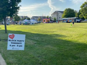 Sign reading Block Party Tonight in foreground with bounce houses, tents, and bus in background