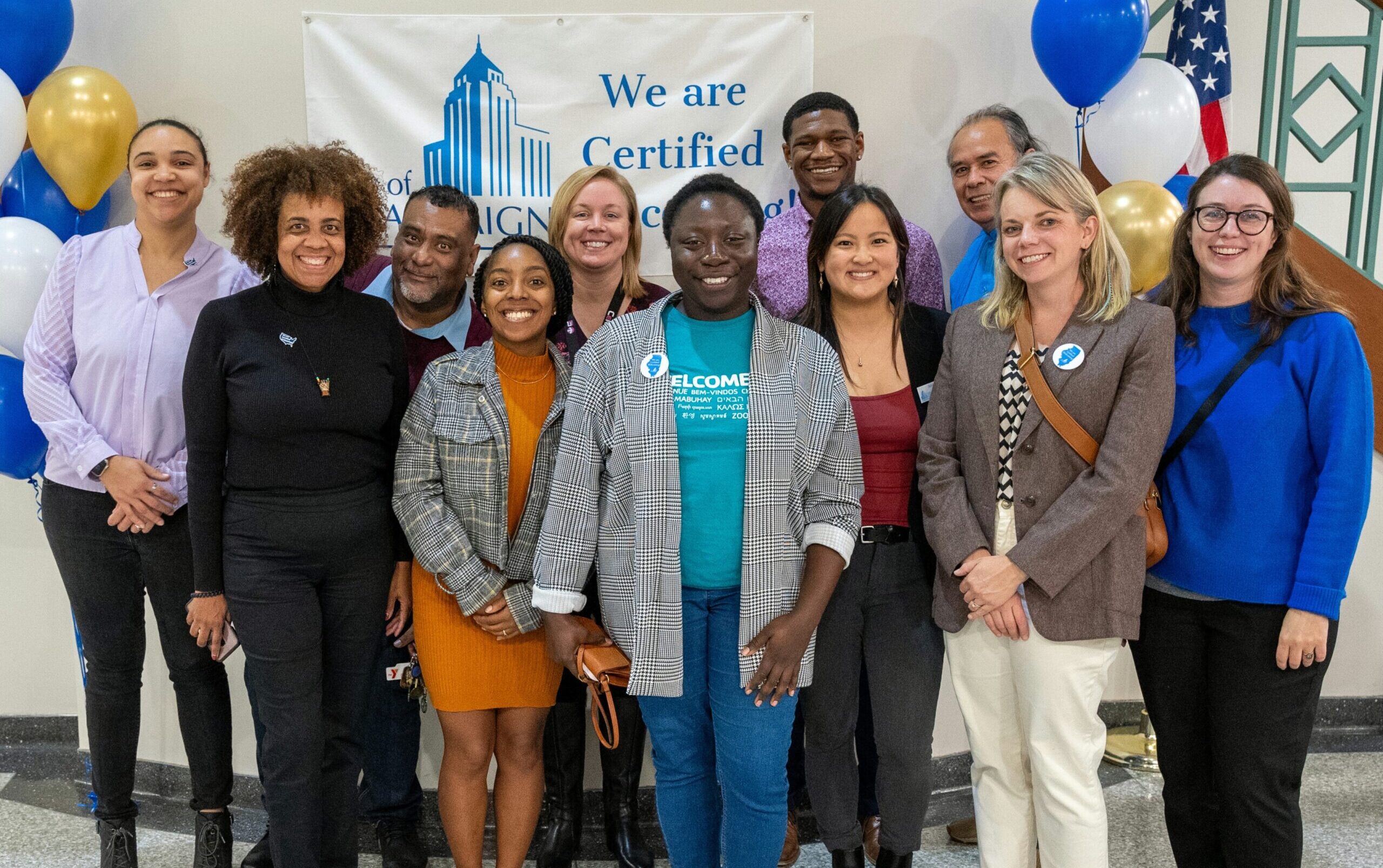 City staff and community partners smiling in front of a banner reading "We are Certified Welcoming."