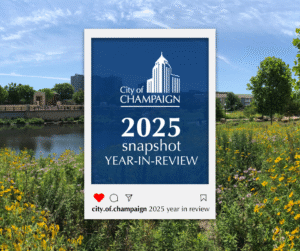 A graphic overlay displays "City of Champaign 2025 snapshot YEAR-IN-REVIEW" over a scenic view of a city skyline, a river, and a field of wildflowers.